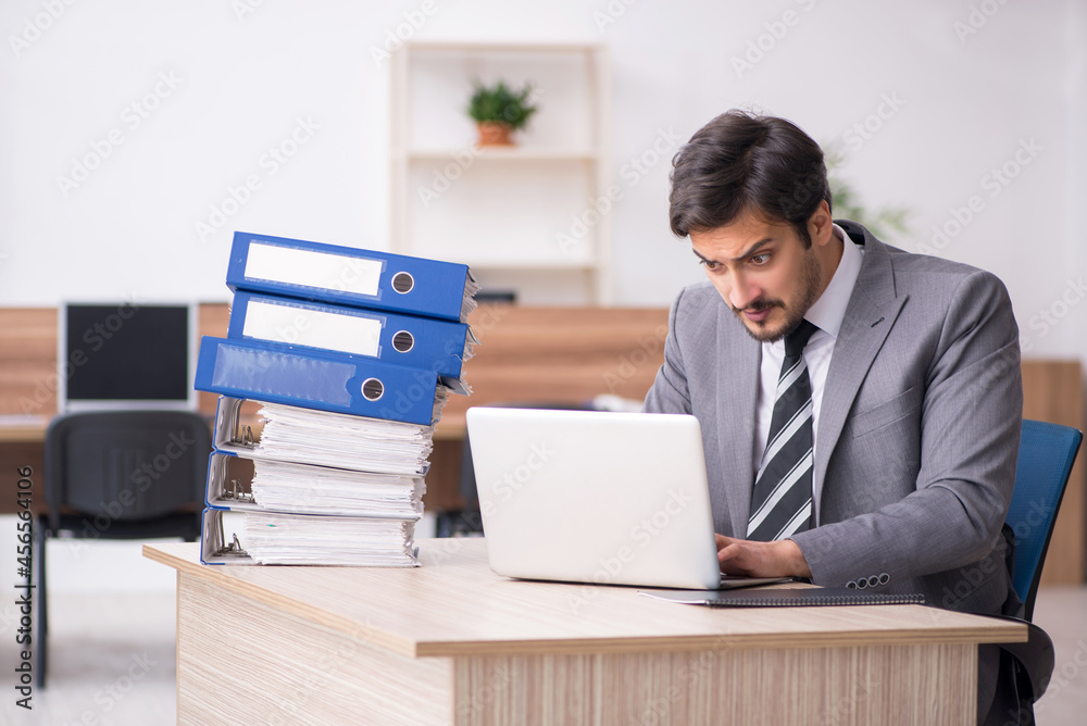 Young male employee unhappy with excessive work in the office Young male employee unhappy with excessive work in the office