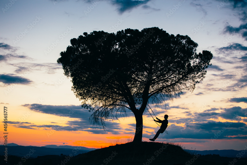 Silhouette of a young woman enjoying freedom at sunset. Tire swinging from a tree outdoors. Holiday concept.