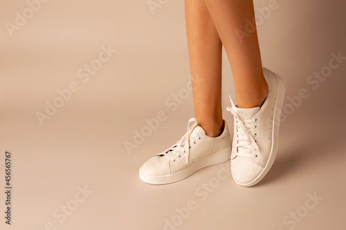 White sneakers shoes and girl’s legs on nude background - casual footwear photo