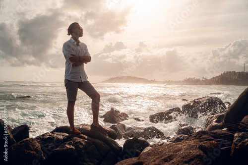 Mężczyzna elegancko ubrany stojący na skałach na tle oceanu i wzburzonych fal.