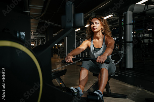 Young athletic woman is engaged in fitness on a rowing machine in the gym in the sunlight. Concept of a healthy lifestyle.