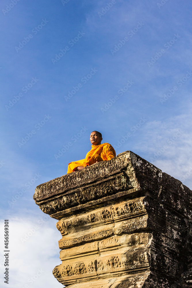 Fototapeta premium Young Buddhist monk sitting outside temple in Angkor Wat, Siem Reap, Cambodia