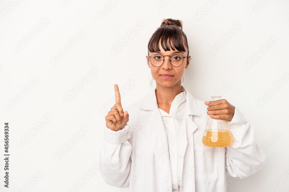Young mixed race scientist woman holding a test tube isolated on white background showing number one with finger. Young mixed race scientist woman holding a test tube isolated on white background showing number one with finger.