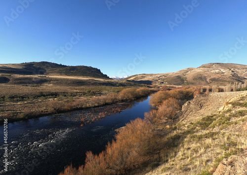Idyllic rural landscape with a clear blue sky. The river flowing across the golden valley, yellow grassland, forest and mountains in autumn. 
