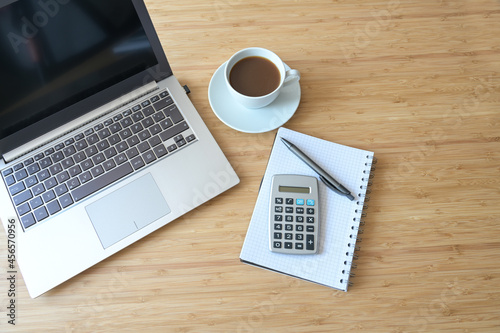 Laptop computer, calculator, spiral book and coffee, flat lay on a wooden desk, business accounting concept, view from above, copy space, selected focus