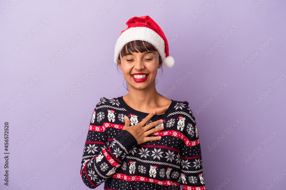 Young mixed race woman celebrating Christmas isolated on purple background laughs out loudly keeping hand on chest. Young mixed race woman celebrating Christmas isolated on purple background laughs out loudly keeping hand on chest.
