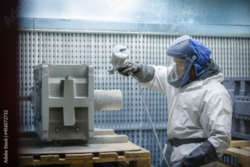 Worker paint spraying industrial gearboxes in factory