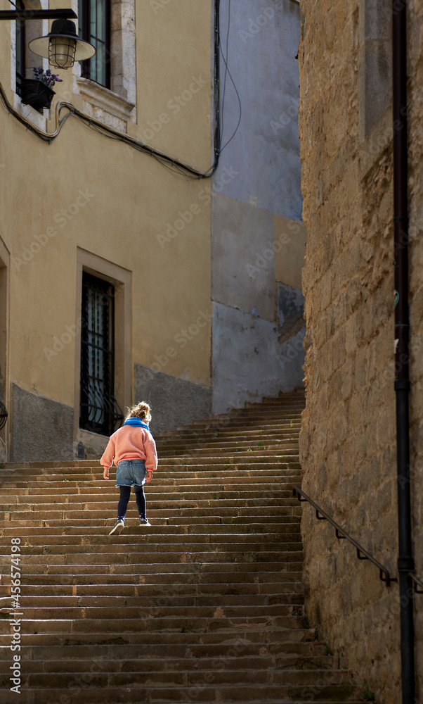 Girl from behind climbing stone stairs with the sun in front on an old street