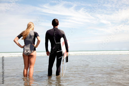 Photography Young couple looking out to sea, young man carrying surfboard