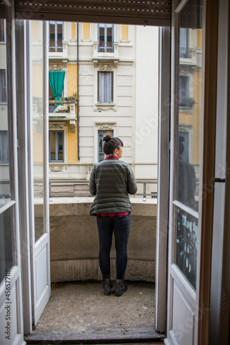 Rear view through doorway of woman standing on balcony, Milan, Italy