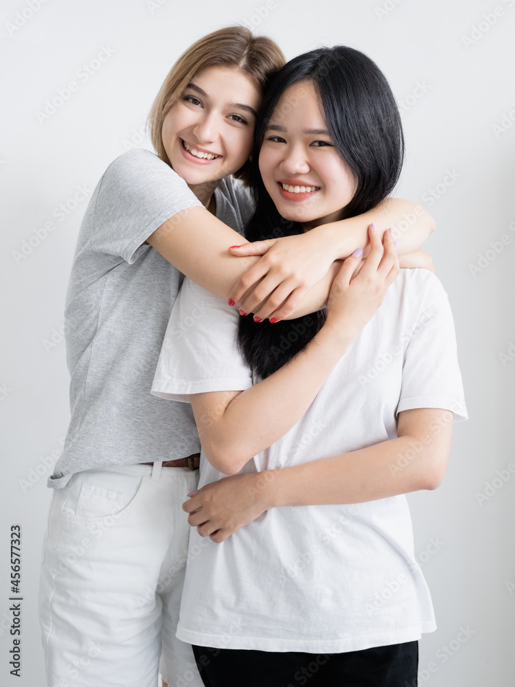 Best female friends. Happy women. Enjoying time. Positive emotions. Pretty caucasian lady embracing asian isolated white. Best female friends. Happy women. Enjoying time. Positive emotions. Pretty caucasian lady embracing asian isolated white.