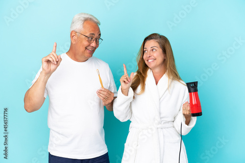 Middle age couple holding dryer and toothbrush isolated on blue background intending to realizes the solution while lifting a finger up