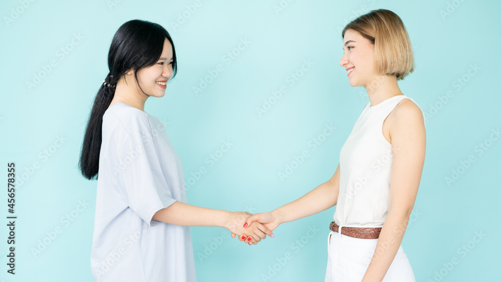 Friendly handshake. Happy women. First meeting. Acquaint gesture. Pretty smiling asian caucasian ladies greeting each other isolated blue. Friendly handshake. Happy women. First meeting. Acquaint gesture. Pretty smiling asian caucasian ladies greeting each other isolated blue.