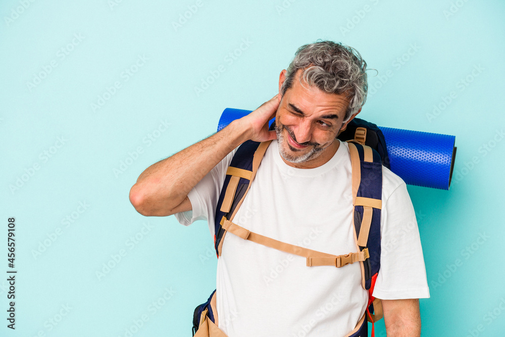 Middle age hiker caucasian man isolated on blue background touching back of head, thinking and making a choice. Middle age hiker caucasian man isolated on blue background touching back of head, thinking and making a choice.