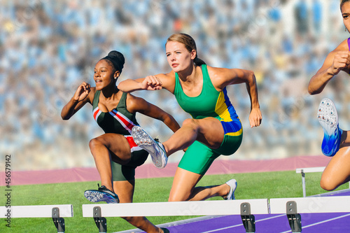 Foto Runners jumping over hurdle on track
