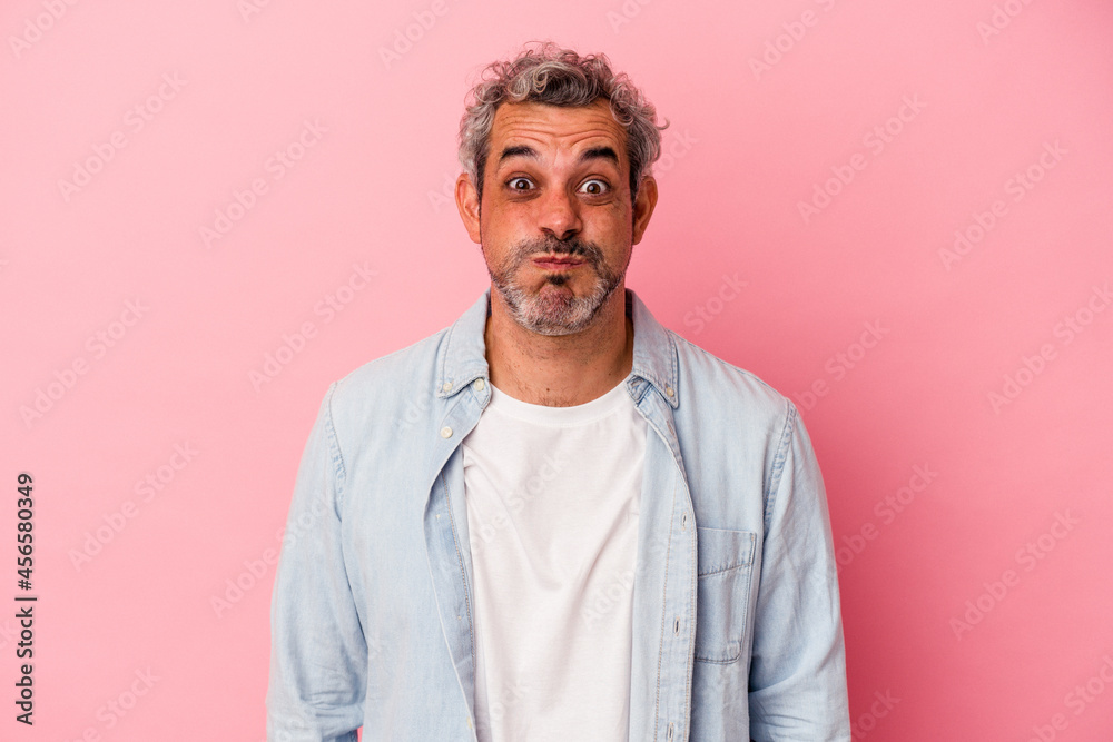 Obraz premium Middle age caucasian man isolated on pink background blows cheeks, has tired expression. Facial expression concept.