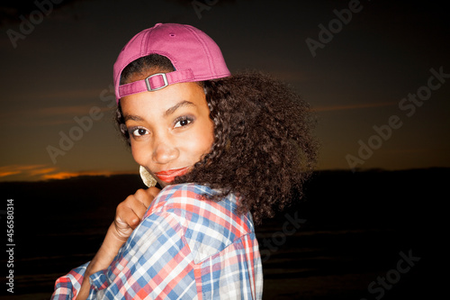 Side view portrait of young woman wearing baseball cap backwards looking at camera smiling