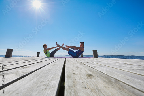 Mid distance view of couple on pier face to face doing sit ups