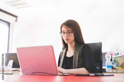 Young woman at office desk typing on laptop