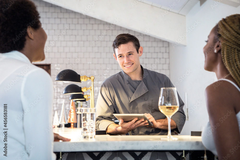 Barman serving customers at bar, barman using digital tablet