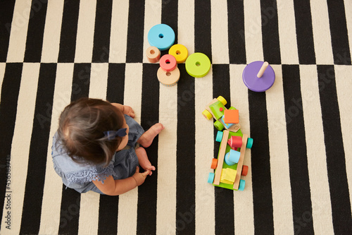 Overhead view of baby girl sitting on rug playing with toy train