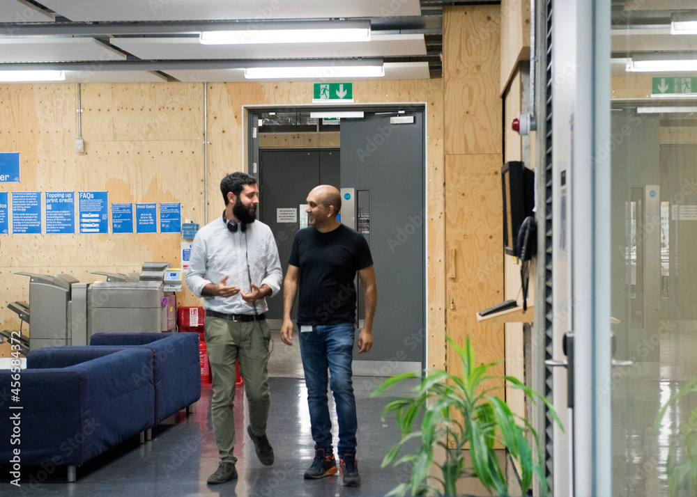 Colleagues walking through office chatting Colleagues walking through office chatting