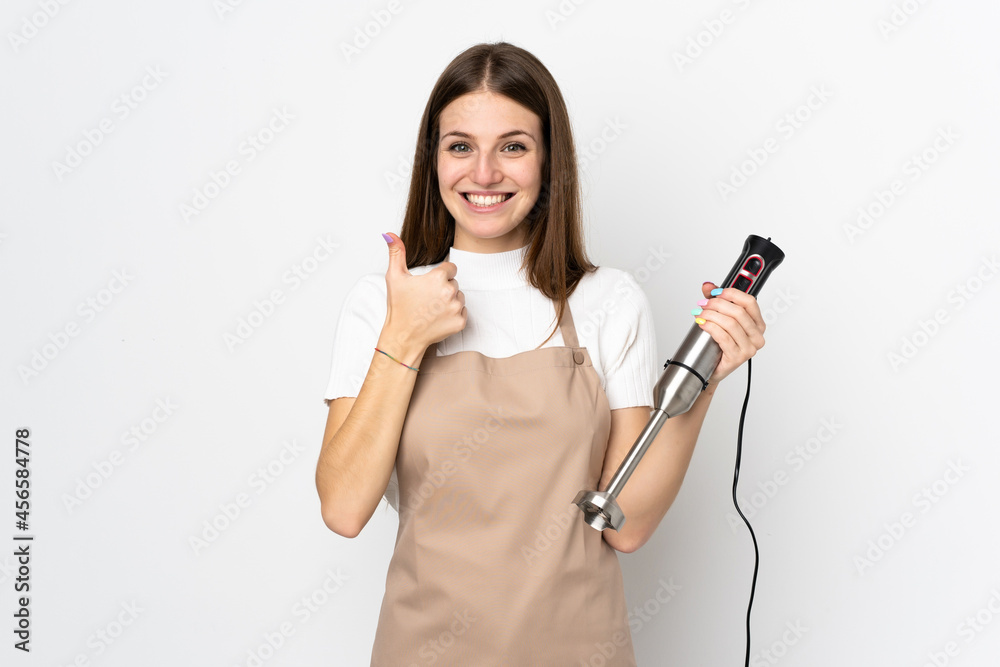 Young woman using hand blender isolated on white background giving a thumbs up gesture Young woman using hand blender isolated on white background giving a thumbs up gesture