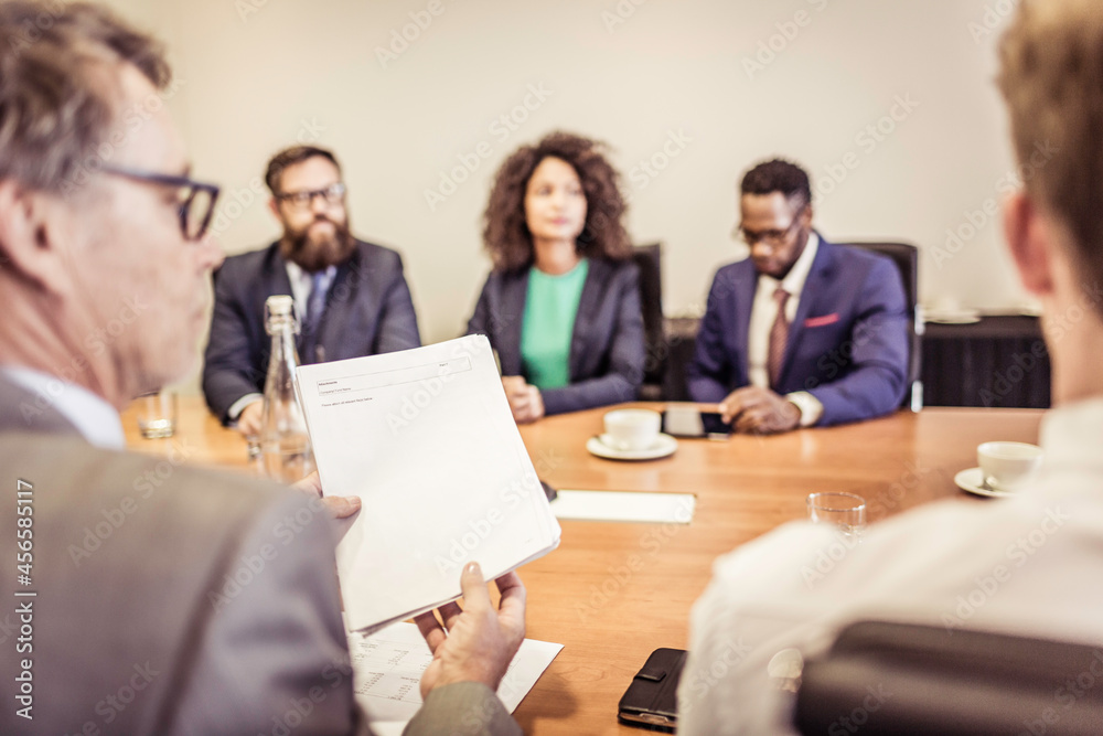 Over the shoulder view of businesswomen and men at conference table meeting Over the shoulder view of businesswomen and men at conference table meeting