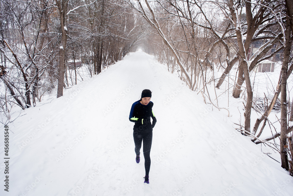 Young female runner in knit hat running in snow covered tree lined park