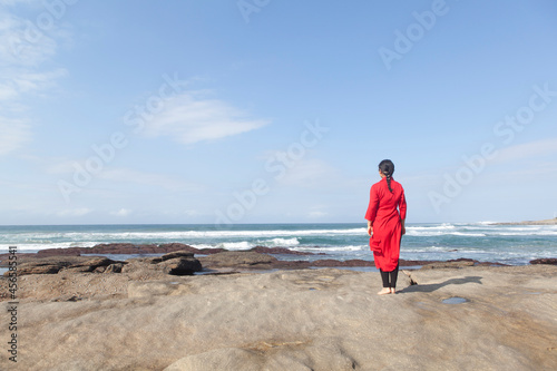 Woman wearing red dress, standing on rocks, looking at sea view, South Africa