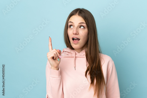 Young caucasian woman isolated on blue background thinking an idea pointing the finger up