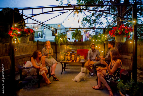 Photography Group of people at garden party, sitting under pergola at dusk, drinking wine