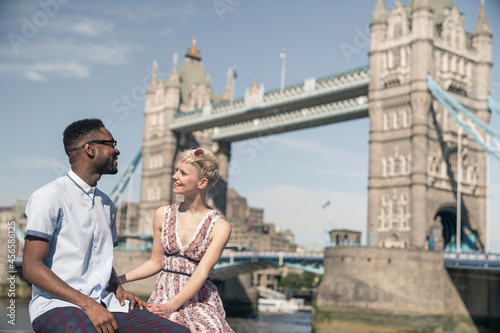 Young couple sitting on wall, smiling, Tower Bridge in background, London, England, UK © Cultura Allies