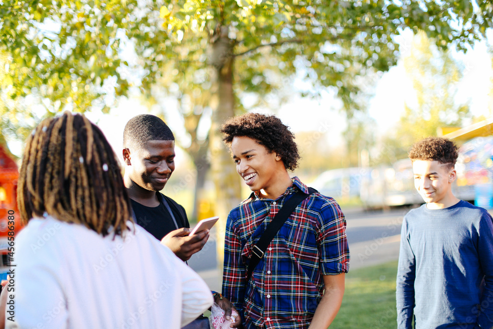 Obraz premium Group of friends in park, boy looking at smartphone, laughing