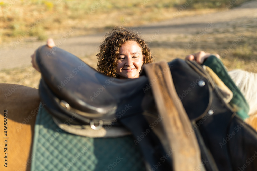 Woman putting saddle on back of horse in countryside Stock Photo