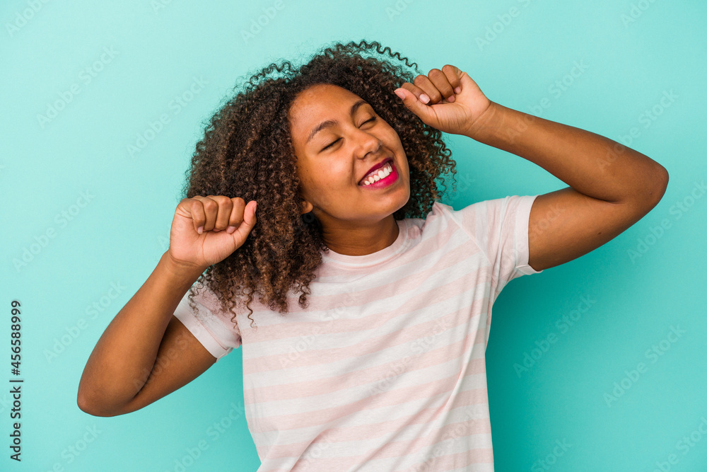 Young african american woman with curly hair isolated on blue background celebrating a special day, jumps and raise arms with energy. Young african american woman with curly hair isolated on blue background celebrating a special day, jumps and raise arms with energy.