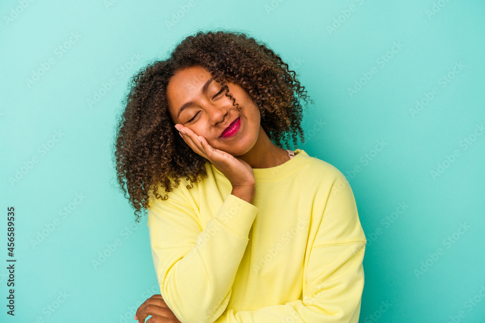 Young african american woman with curly hair isolated on blue background who is bored, fatigued and need a relax day. Young african american woman with curly hair isolated on blue background who is bored, fatigued and need a relax day.