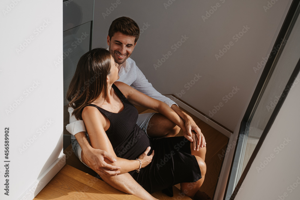 Smiling man embracing pregnant wife while talking in house Smiling man embracing pregnant wife while talking in house