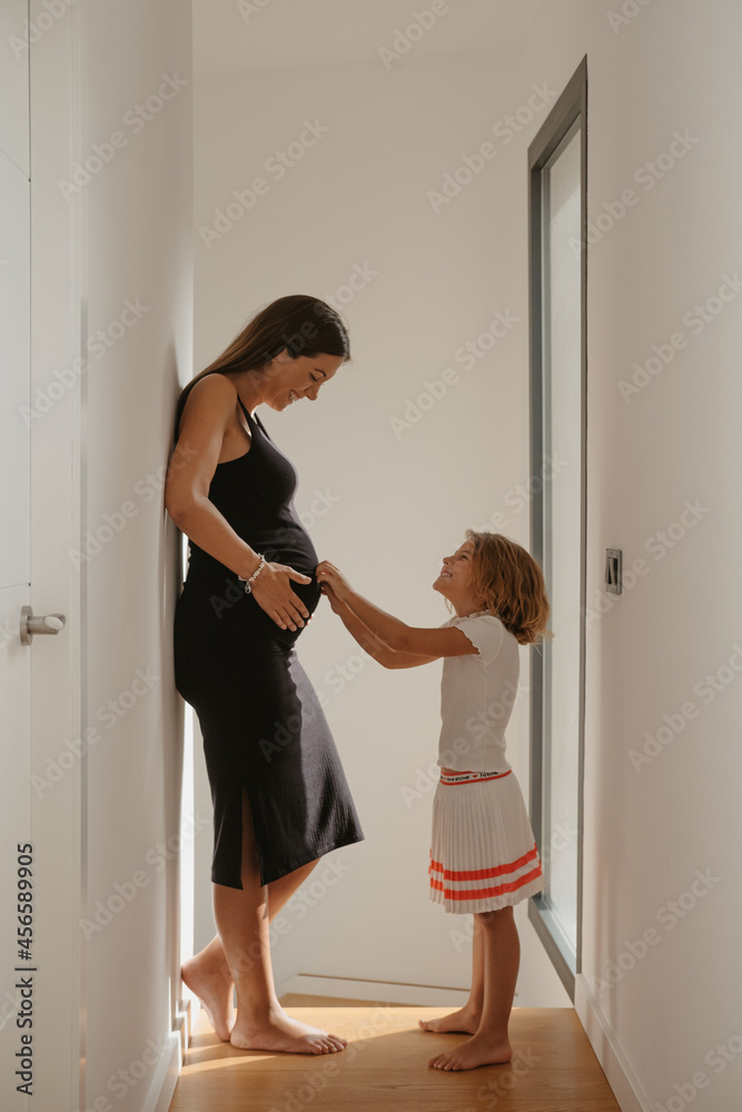 Smiling girl touching tummy of pregnant mother in hallway Smiling girl touching tummy of pregnant mother in hallway