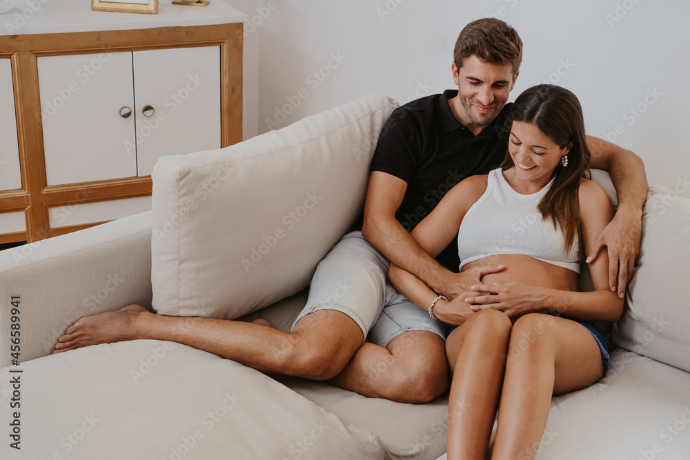 Husband embracing pregnant wife on sofa at home Husband embracing pregnant wife on sofa at home