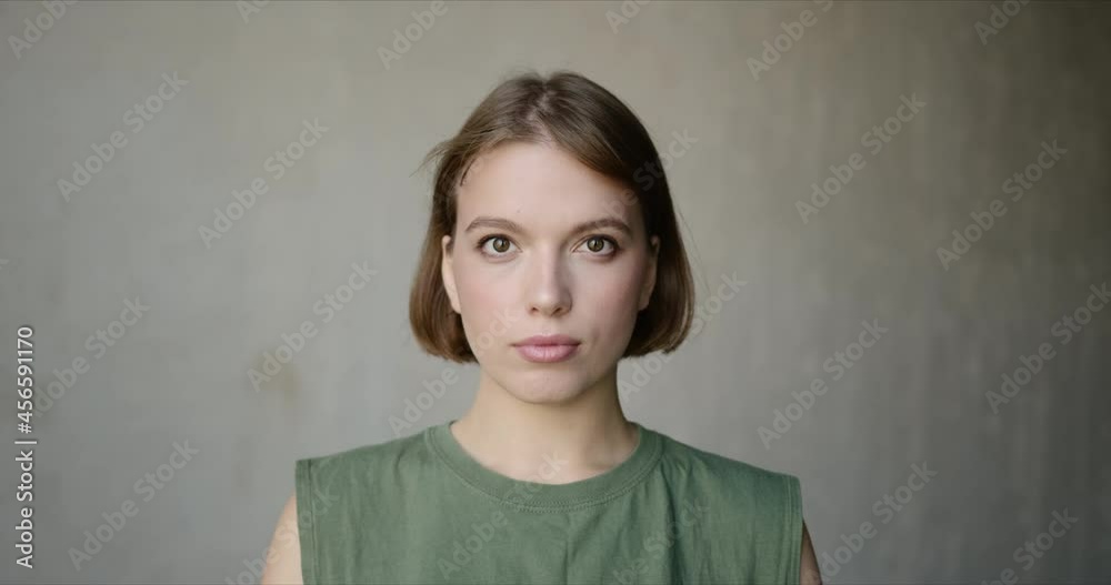 Slow motion of young woman looking at camera, smiling and laughing with natural face expression. Beautiful girl standing alone against wall Slow motion of young woman looking at camera, smiling and laughing with natural face expression. Beautiful girl standing alone against wall