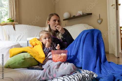 Tochter und Mutter schauen gemeinsam eingekuschelt Fernsehen und essen dabei Popcorn photo