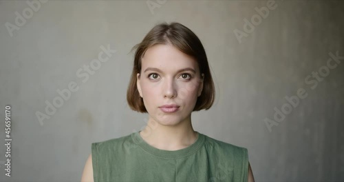 Slow motion of young woman looking at camera, smiling and laughing with natural face expression. Beautiful girl standing alone against wall