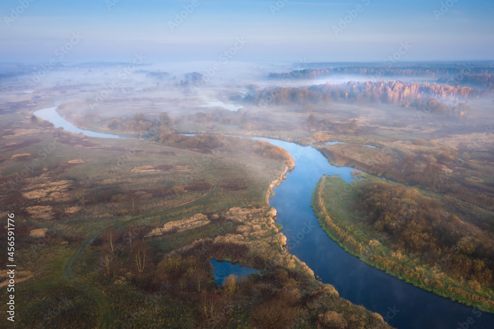 Aerial view of scenic contryside in autumn season. Misty sunrise above narrow river.
