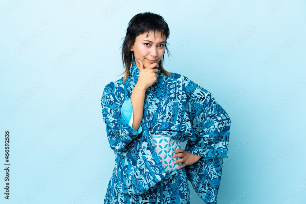 Young woman wearing kimono over isolated blue background having doubts Young woman wearing kimono over isolated blue background having doubts