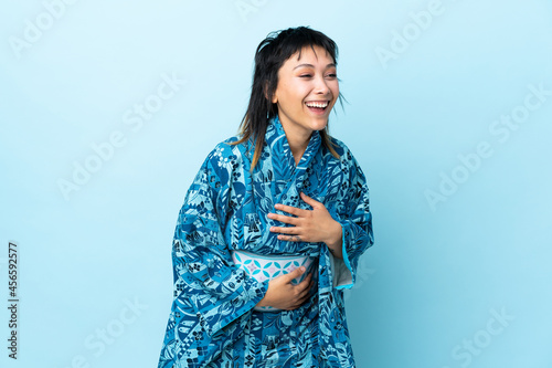 Young woman wearing kimono over isolated blue background smiling a lot