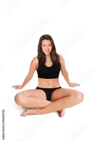 Smiling young woman wearing a black bikini in front of white studio background 
