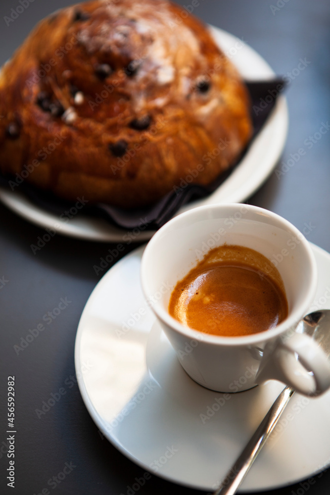The table with sweets (pastries: croissant, cookies), white cups (mug) with hot black coffee (espresso), the saucer, the spoons at a local bar. Traditional Italian breakfast. Milan, Lombardy, Italy The table with sweets (pastries: croissant, cookies), white cups (mug) with hot black coffee (espresso), the saucer, the spoons at a local bar. Traditional Italian breakfast. Milan, Lombardy, Italy