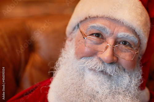 Portrait of smiling kind senior Santa Claus with white beard and eyebrows wearing eyeglasses and cap