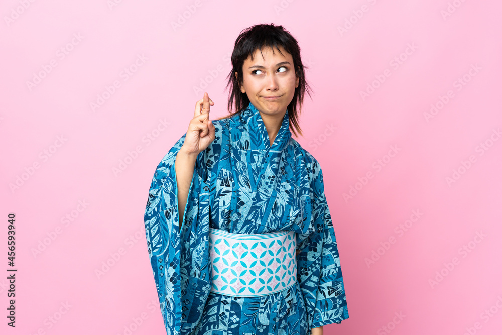 Young woman wearing kimono over isolated blue background with fingers crossing and wishing the best Young woman wearing kimono over isolated blue background with fingers crossing and wishing the best